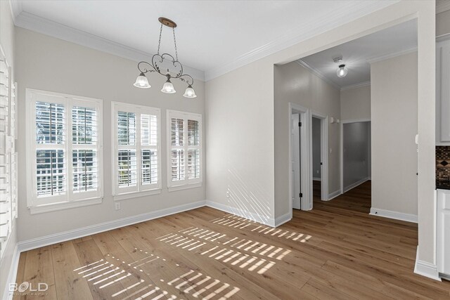 unfurnished dining area with hardwood / wood-style flooring, crown molding, and an inviting chandelier