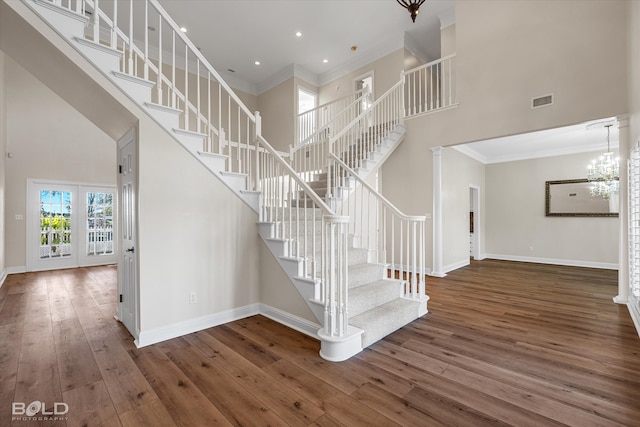 stairs with a notable chandelier, wood-type flooring, ornamental molding, and a high ceiling