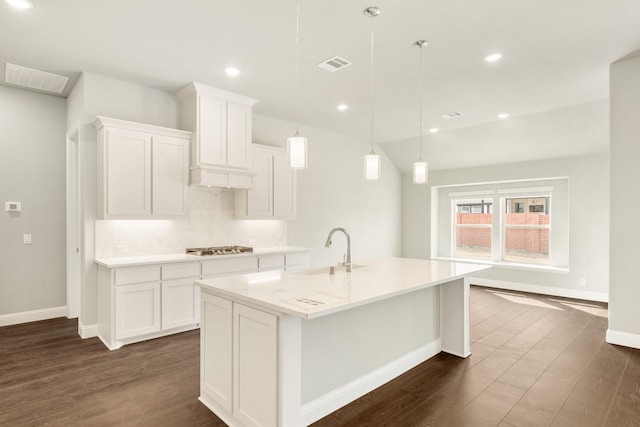 kitchen featuring a sink, visible vents, tasteful backsplash, and an island with sink