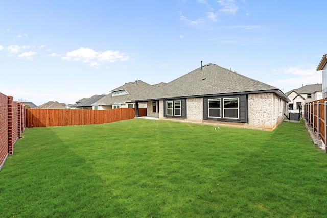 rear view of house with a fenced backyard, brick siding, a yard, and a shingled roof