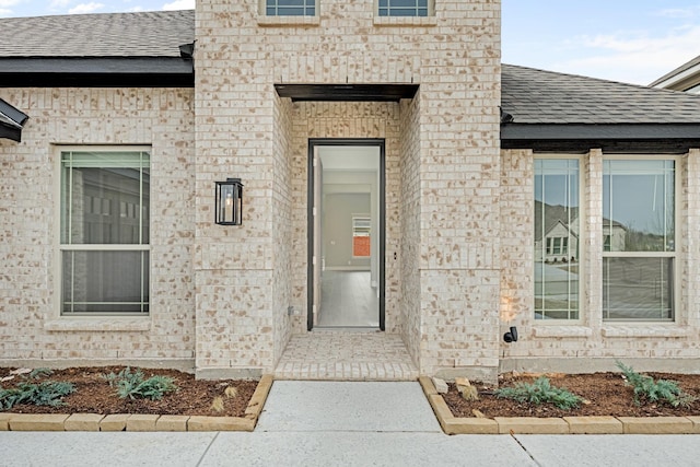 doorway to property with brick siding and roof with shingles