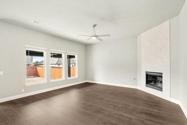 unfurnished living room featuring visible vents, dark wood-type flooring, a premium fireplace, baseboards, and ceiling fan