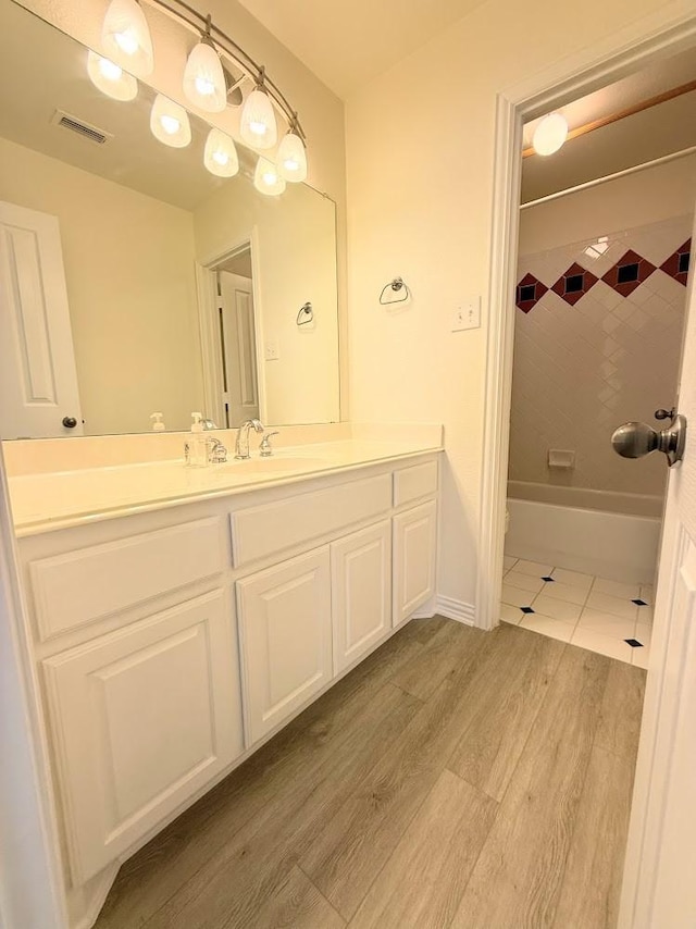 bathroom with hardwood / wood-style floors, vanity, and tiled shower / bath