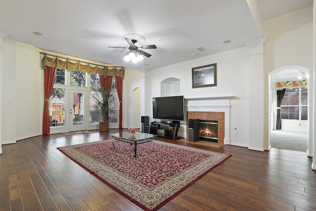 living room with a tile fireplace, ceiling fan, and dark wood-type flooring