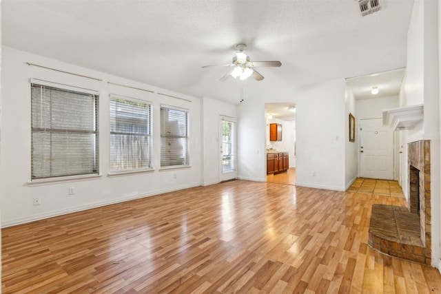 unfurnished living room with a brick fireplace, ceiling fan, a textured ceiling, and light wood-type flooring