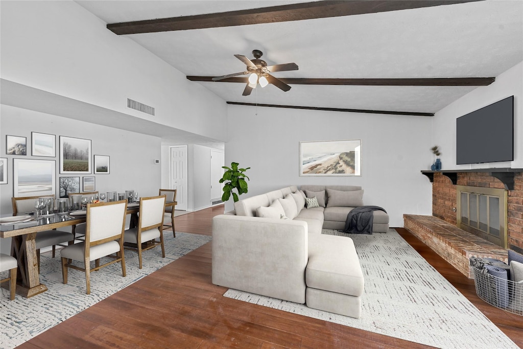 living area featuring vaulted ceiling with beams, a fireplace, visible vents, a ceiling fan, and wood finished floors