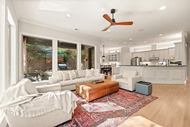 living room with sink, crown molding, ceiling fan, and light wood-type flooring