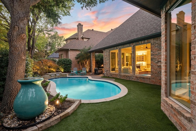 pool at dusk with a patio area and a lawn