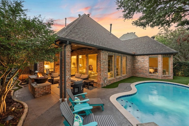 pool at dusk featuring a patio and an outdoor living space with a fireplace