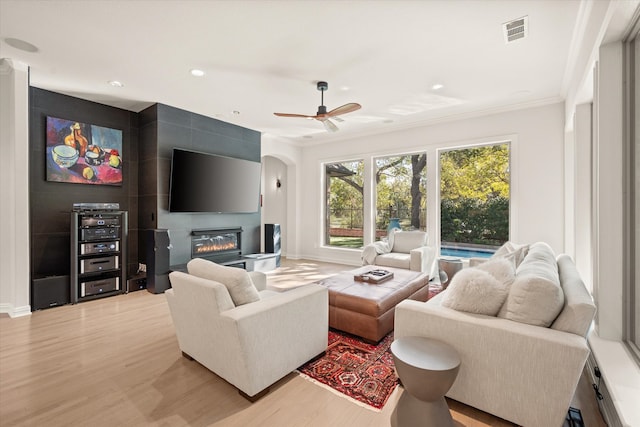 living room with crown molding, ceiling fan, a fireplace, and light wood-type flooring