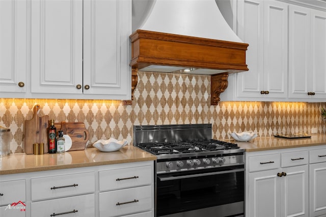 kitchen with white cabinets, backsplash, stainless steel gas range oven, and premium range hood