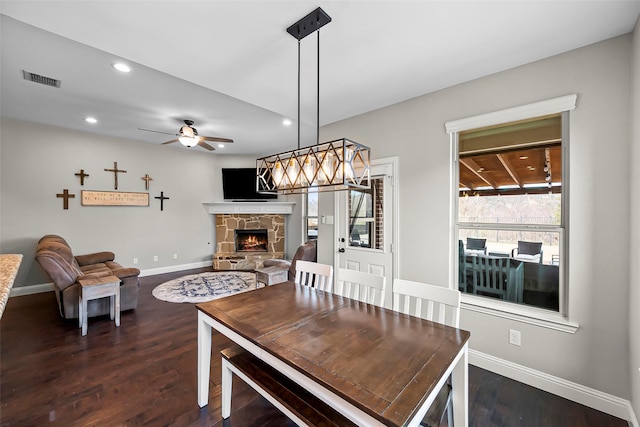 dining area featuring a stone fireplace, dark hardwood / wood-style floors, and ceiling fan