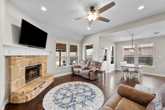 living room featuring vaulted ceiling, a stone fireplace, dark hardwood / wood-style floors, and ceiling fan