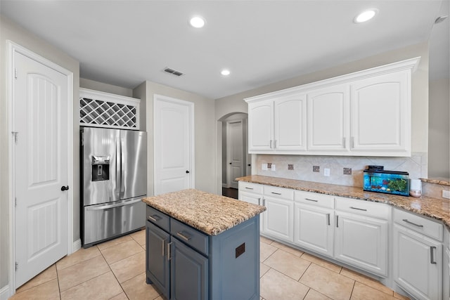 kitchen featuring stainless steel fridge, light stone countertops, a kitchen island, and white cabinets