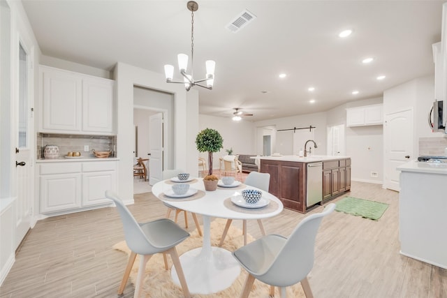 dining space with visible vents, a barn door, recessed lighting, light wood-style flooring, and ceiling fan with notable chandelier