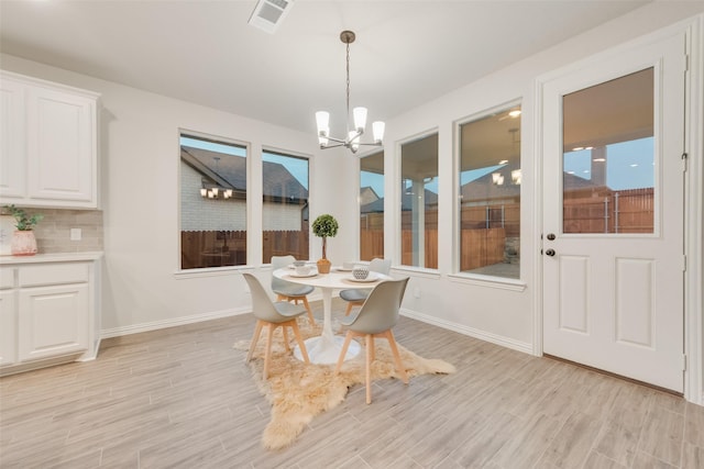 dining space with baseboards, visible vents, light wood finished floors, and a chandelier