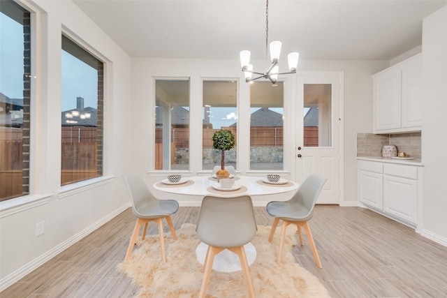 dining area with light wood finished floors, a notable chandelier, plenty of natural light, and baseboards