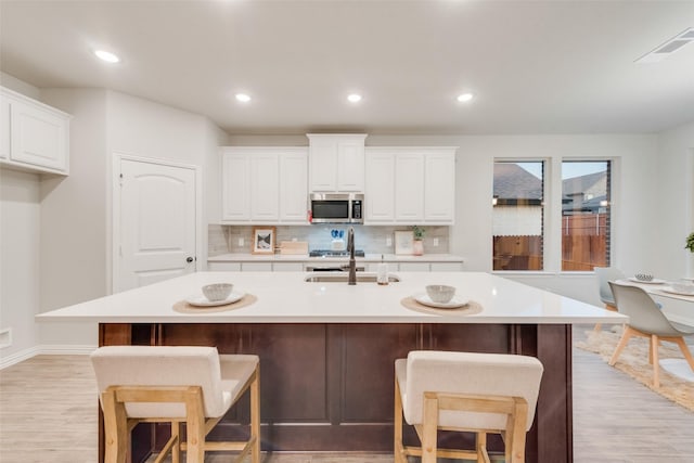 kitchen featuring a sink, light countertops, stainless steel microwave, range, and tasteful backsplash