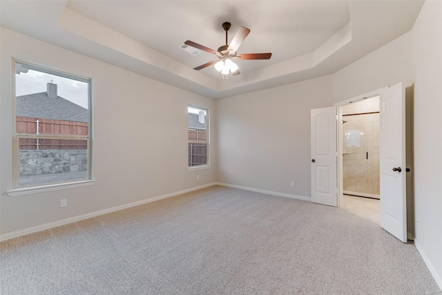 spare room with a tray ceiling, baseboards, visible vents, and light carpet