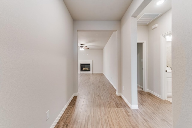 hall featuring light wood-type flooring, baseboards, and visible vents