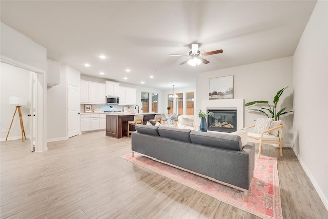 living room featuring recessed lighting, light wood-type flooring, baseboards, and a glass covered fireplace