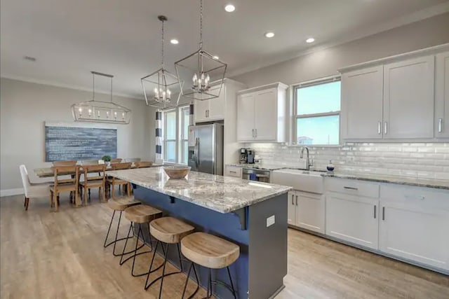 kitchen featuring white cabinetry, light stone countertops, decorative light fixtures, a kitchen island, and appliances with stainless steel finishes