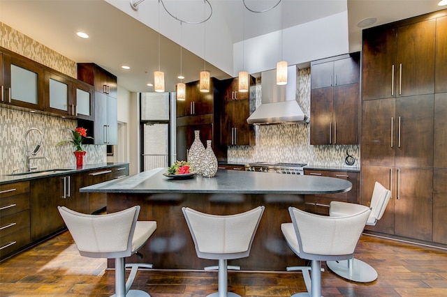 kitchen with dark hardwood / wood-style flooring, sink, wall chimney range hood, stainless steel stove, and a kitchen island