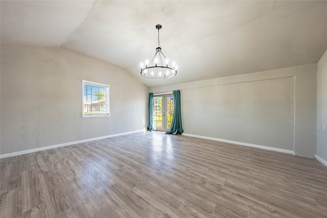 spare room with hardwood / wood-style floors, an inviting chandelier, and vaulted ceiling