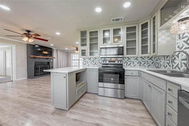 kitchen with sink, light hardwood / wood-style flooring, a brick fireplace, appliances with stainless steel finishes, and kitchen peninsula