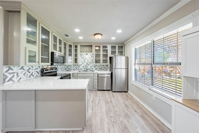 kitchen featuring stainless steel appliances, light hardwood / wood-style flooring, kitchen peninsula, decorative backsplash, and ornamental molding