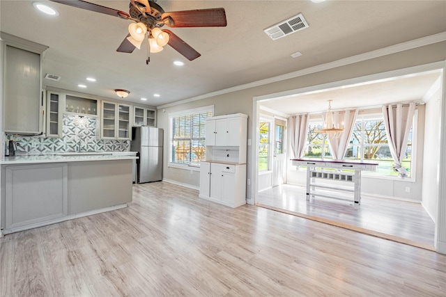 kitchen with tasteful backsplash, stainless steel refrigerator, crown molding, and light hardwood / wood-style flooring