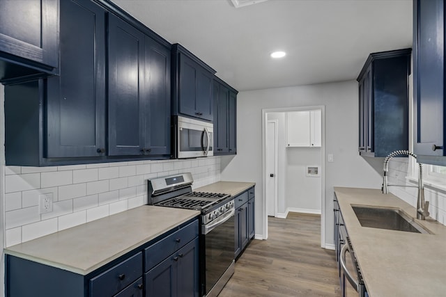 kitchen featuring appliances with stainless steel finishes, tasteful backsplash, blue cabinets, sink, and wood-type flooring