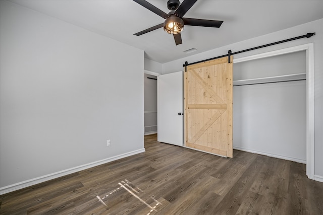 unfurnished bedroom with ceiling fan, a barn door, dark hardwood / wood-style flooring, and a closet