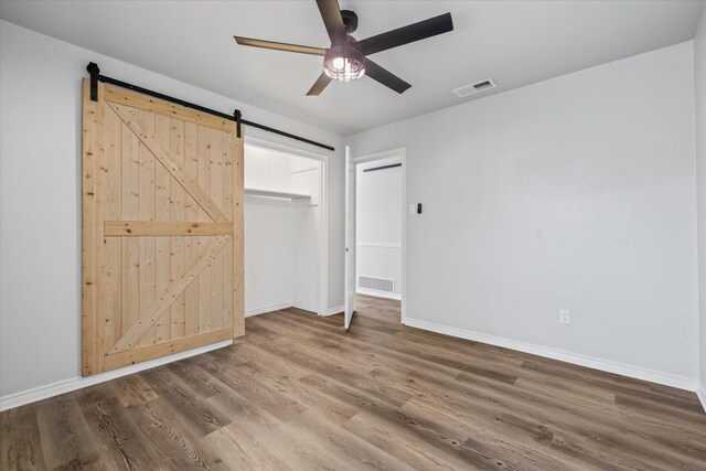 unfurnished bedroom featuring a barn door, ceiling fan, a closet, and wood-type flooring