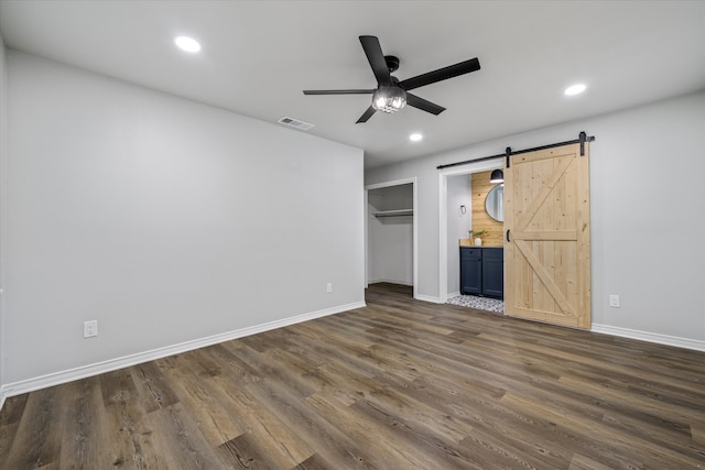 unfurnished bedroom with ceiling fan, a barn door, dark hardwood / wood-style floors, ensuite bathroom, and a closet