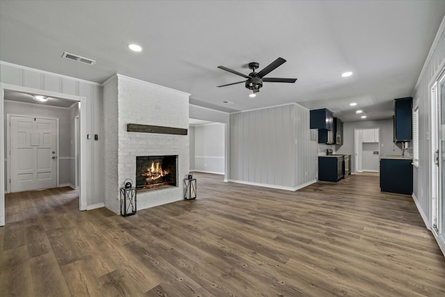 unfurnished living room featuring ceiling fan, dark hardwood / wood-style flooring, ornamental molding, and a brick fireplace