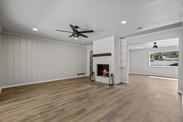 unfurnished living room with ceiling fan, crown molding, hardwood / wood-style flooring, a fireplace, and wood walls