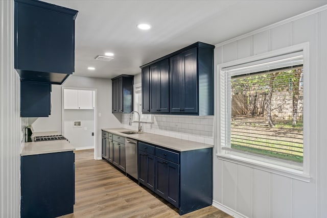 kitchen featuring sink, light wood-type flooring, blue cabinetry, tasteful backsplash, and stainless steel appliances