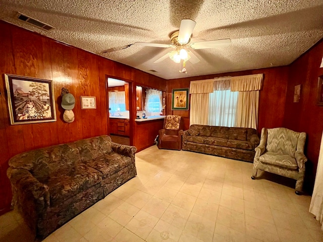 living room with a textured ceiling, ceiling fan, and wood walls