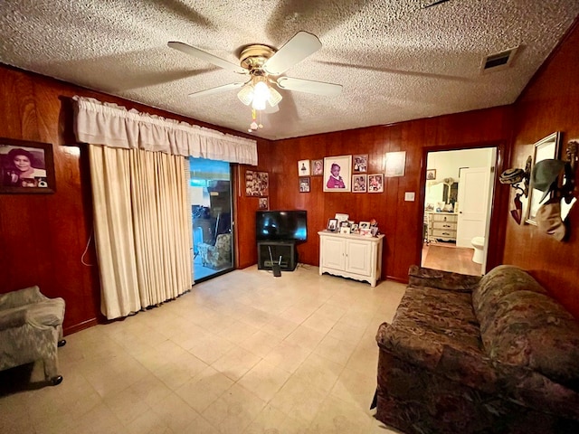 living room with ceiling fan, wooden walls, and a textured ceiling