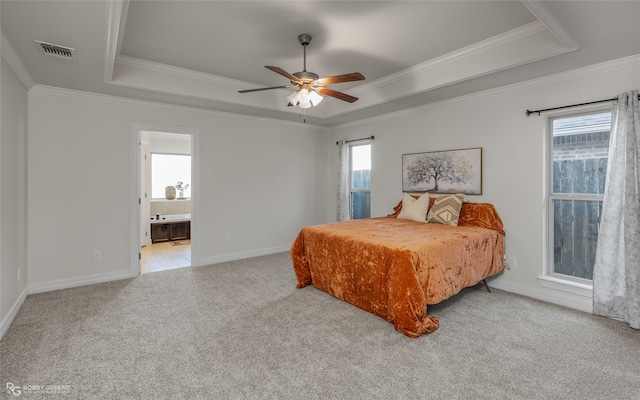 carpeted bedroom featuring a raised ceiling, ensuite bath, multiple windows, and ceiling fan