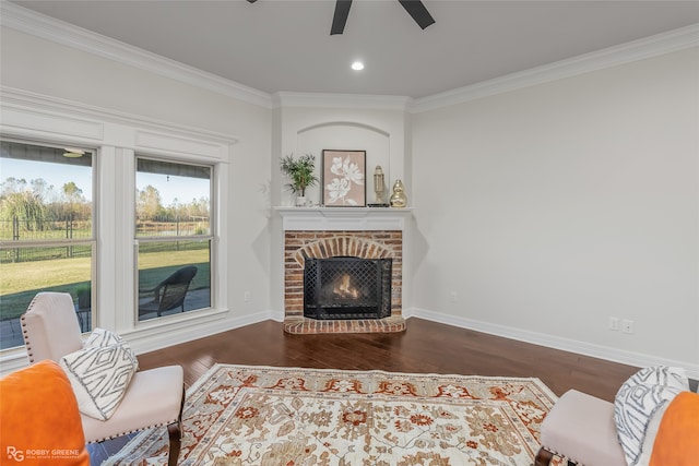 living room with dark hardwood / wood-style floors, ceiling fan, ornamental molding, and a brick fireplace