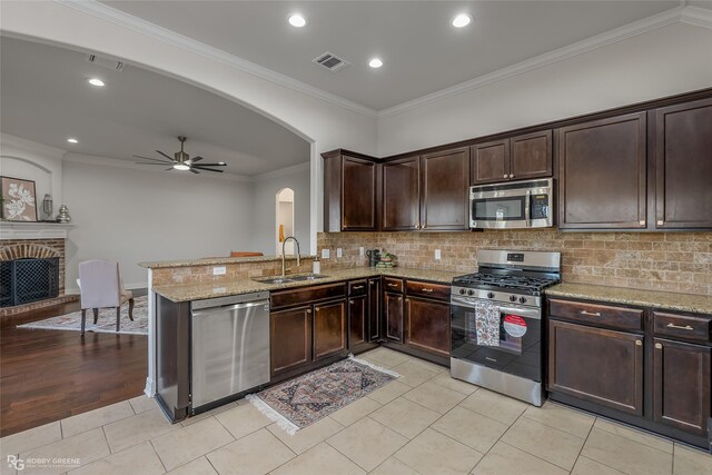 kitchen with crown molding, sink, a fireplace, appliances with stainless steel finishes, and kitchen peninsula