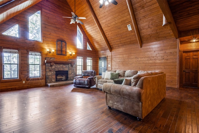 living room with beamed ceiling, a stone fireplace, dark wood-type flooring, and wooden walls