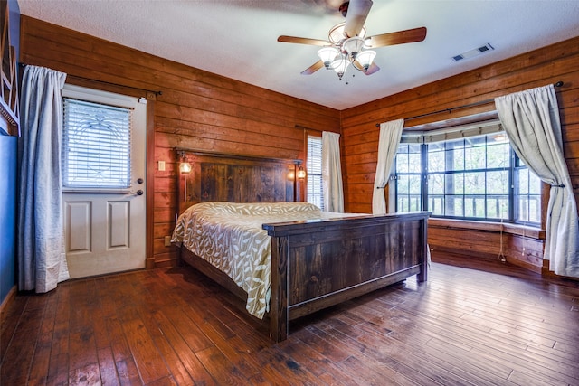 bedroom featuring a textured ceiling, ceiling fan, dark wood-type flooring, and wood walls