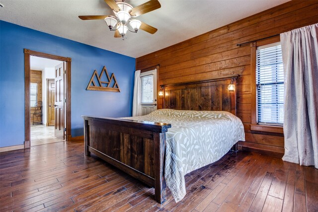 bedroom with ceiling fan, wood walls, dark hardwood / wood-style floors, and multiple windows