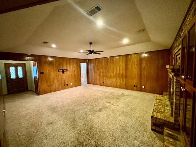 unfurnished living room with a textured ceiling, light colored carpet, ceiling fan, and wooden walls