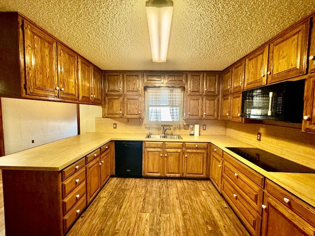 kitchen with kitchen peninsula, light wood-type flooring, a textured ceiling, sink, and black appliances