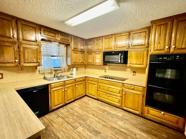 kitchen featuring sink, black appliances, a textured ceiling, and light hardwood / wood-style flooring