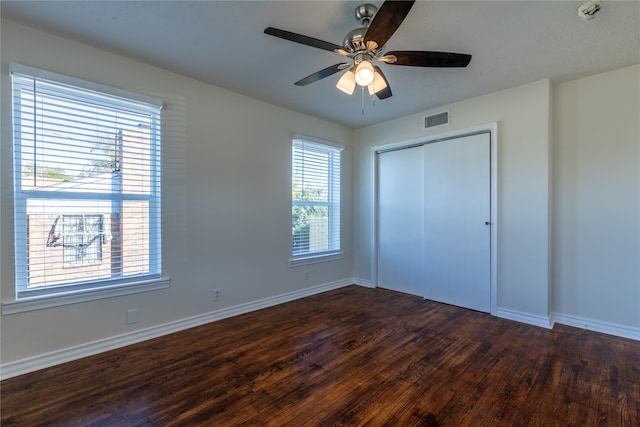 unfurnished bedroom featuring a closet, multiple windows, dark wood-type flooring, and ceiling fan